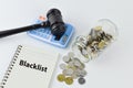 Phrase BLACKLIST written on notebook with judge gavel, calculator and coins