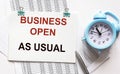 The phrase Business as usual printed on a notebook. Documents, alarm clock and pen lie on a white background Royalty Free Stock Photo