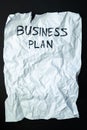 Phrase `business plan` handwritten on crumpled torn paper, top view.