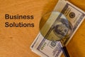 Phrase BUSINESS SOLUTIONS written on board with magnifying glass and money banknotes Royalty Free Stock Photo