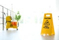 Phrase CAUTION WET FLOOR on safety sign and yellow mop bucket with cleaning supplies, indoors Royalty Free Stock Photo
