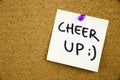 A yellow sticky note writing, caption, inscription Phrase CHEER UP in black ext on a sticky note pinned to a cork notice Royalty Free Stock Photo