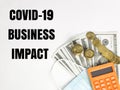 Phrase COVID-19 BUSINESS IMPACT with calculator, face mask, coins and dollar bank notes.