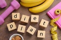 Phrase Diet Plan made of cubes, fitness items and products on wooden table, flat lay. Weight loss concept