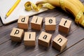 Phrase Diet Plan made of cubes, measuring tape and bananas on grey wooden table. Weight loss program