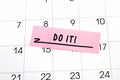 The phrase Do it written on a pink sticky note posted on a calendar or planner page. Deadline concept read a reminder on calendar Royalty Free Stock Photo