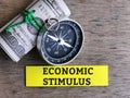 Phrase ECONOMIC STIMULUS written on sticky note with fake money and compass.