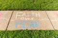 The phrase `Faith over Fear` written with sidewalk chalk on gray concrete pavement background