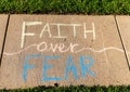 The phrase `Faith over Fear` written with sidewalk chalk on gray concrete pavement background