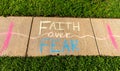 The phrase `Faith over Fear` written with sidewalk chalk on gray concrete pavement background