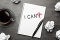 Phrase I CAN`T with crossed out letter T written in notebook, pen, crumpled paper and coffee on grey table, flat lay. Motivation Royalty Free Stock Photo