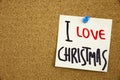 A yellow sticky note writing, caption, inscription Phrase I LOVE CHRISTMAS in black ext on a sticky note pinned to a cork notice b Royalty Free Stock Photo