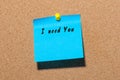 The phrase I need you written on blue sticker pinned to a cork notice board