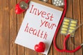 Phrase Invest your health written on sheet of paper, stethoscope and pills on wooden background