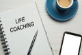 Phrase Life Coaching written in notebook, pen, smartphone and cup coffee on white wooden table, flat lay Royalty Free Stock Photo