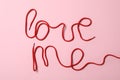 Phrase Love Me made with red shoe laces on pink background, flat lay
