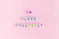 Phrase `Love yourself` made out of beads on pastel pink background