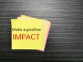 Phrase make a positive impact written on sticky note on the table.