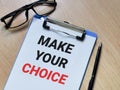 Phrase MAKE YOUR CHOICE written on paper clipboard with pen and eye glasses. Royalty Free Stock Photo