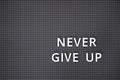 Phrase Never Give Up spelled out with white letters on gray pegboard