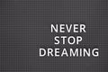 Phrase Never Stop Dreaming spelled out with white letters on gray pegboard