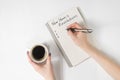 Phrase New Year`s resolutions in the notebook. Female hand with pen and cup of coffee