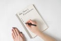 Phrase New Year`s resolutions in the notebook. Female hands with pen