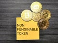 Phrase non fungible token written on sticky note with golden bitcoins.