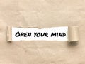 Phrase OPEN YOUR MIND appearing behind torn brown paper. Royalty Free Stock Photo