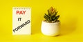 The phrase Pay It Forward with text on a white notepad, placed on a yellow background Royalty Free Stock Photo