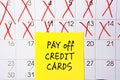 The phrase Pay off Credit cards written in black text on a yellow sticky note posted to a calendar page as a reminder. Close up of Royalty Free Stock Photo