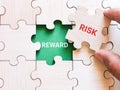 Phrase risk reward written on jigsaw puzzle with hand.