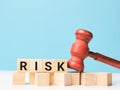 Phrase RISK on wooden cubes with gavel on blue background.