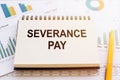 The phrase Severance Pay is written in a notepad that lies on a table with financial charts and diagrams. Business concept