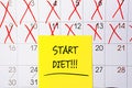 The phrase Start Diet written in black text on a yellow sticky note posted to a calendar page as a reminder. Close up of a Royalty Free Stock Photo