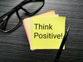 Phrase think positive written on sticky note with a pen and eye glasses.