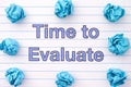 The phrase Time To Evaluate written on a lined notebook sheet with some crumpled paper balls around it