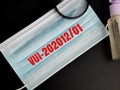 Phrase VUI-202012 01 on disposal face mask with hand sanitizer and magnifying glass isolated on black background.