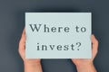 The phrase where to invest is standing on a paper, hands holding the question