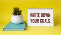 Phrase Write down your goals written on notepad and yellow background with green diary and cactus flower. Goals and plans