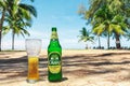 Phuket, Thailand - Mart 6, 2018: Bottle and glass of cold Chang beer on the sand on the background of green palm trees.