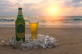 Misted bottle and glass of cold beer on the sand of scenic at the background of seascape, sunset sky and sea waves. Royalty Free Stock Photo