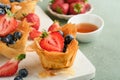 Phyllo or filo pies with fresh berries strawberries and blueberries, cheese filling topped with fresh mint on white plate.