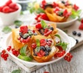 Phyllo pastry fruit cups with whipped cream filling topped with mix fresh berries sprinkled with powder sugar on a white plate clo