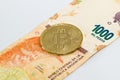 Physical Bitcoin over a thousand argentinian pesos bill on white background. Cryptocurrency exchange, investment concept