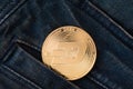 A physical golden Dash cryptocurrency coin sticks out of the pocket of blue frayed jeans.