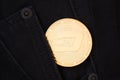 A physical golden Dash cryptocurrency coin sticks out of the pocket of dark jeans.