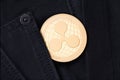 A physical golden Ripple coin sticks out of the pocket of black jeans close-up.