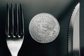 Physical silver Crytocurrency Coin between fork and knive.