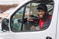 Physical working - package delivery. Positive smiling African-American man in black baseball hat sitting on driver& x27;s Royalty Free Stock Photo